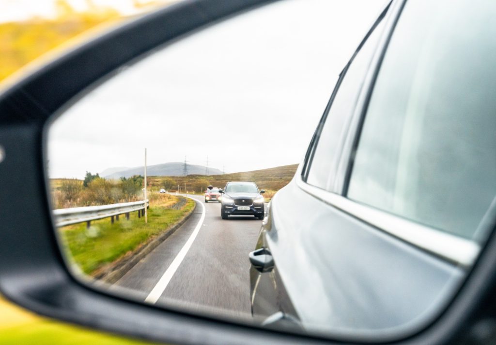 A reflection in a car side mirror showing drivers tailgating or driving too closely behind.