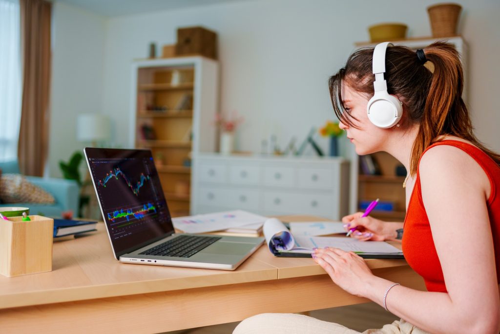 A young female student studying in front of her laptop wearing headphones.