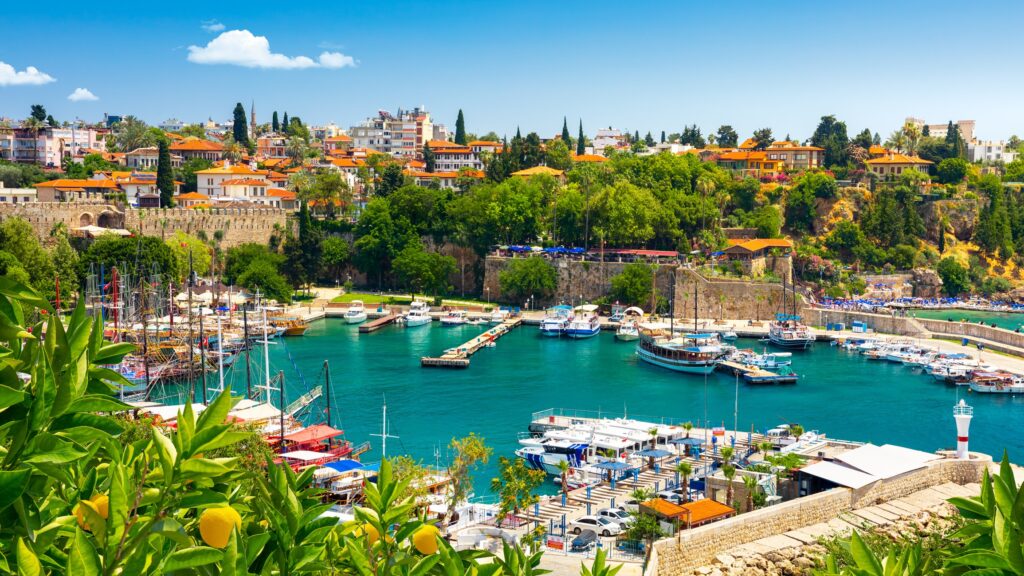 A bright and sunny Turkish harbour with boats and green trees visible.