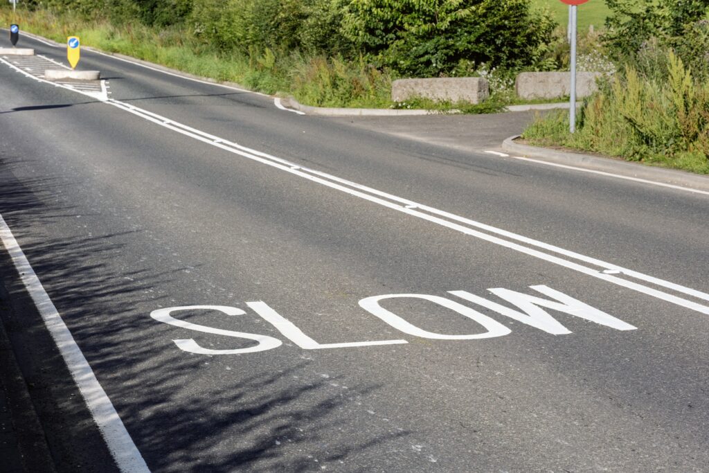 A country road with 'slow' written and a solid white line visible for no overtaking.