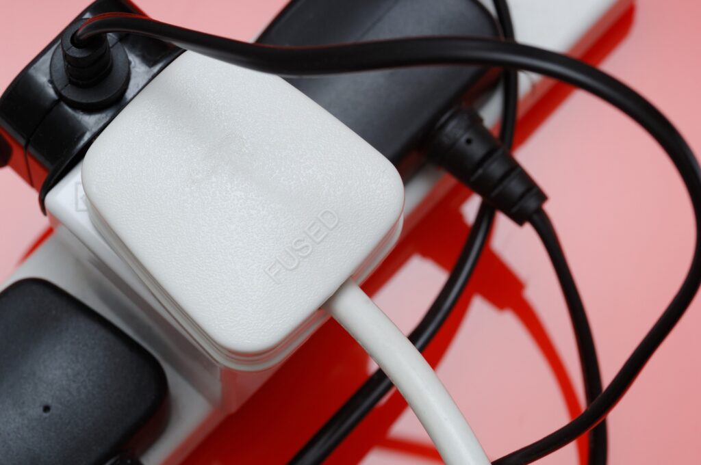 A UK extension cable overloaded with white and black plugs on a bright red table.