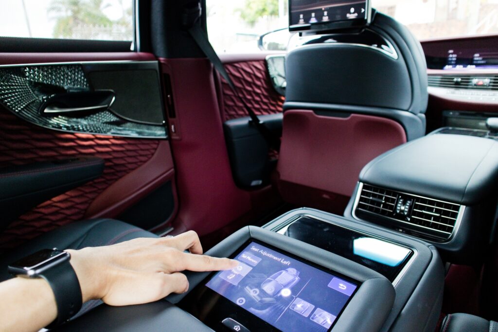 An internal shot of a modern car with red and black upholstery with the driver reviewing the car set up options on a digital touchscreen.