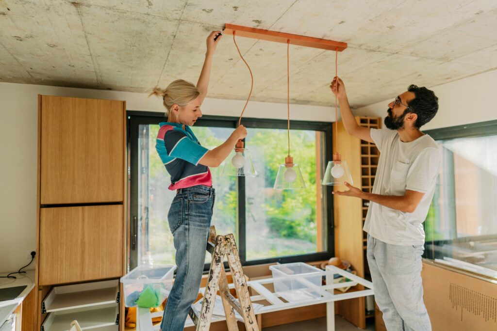 A young couple fixing up their home, visible in the kitchen installing a new light.
