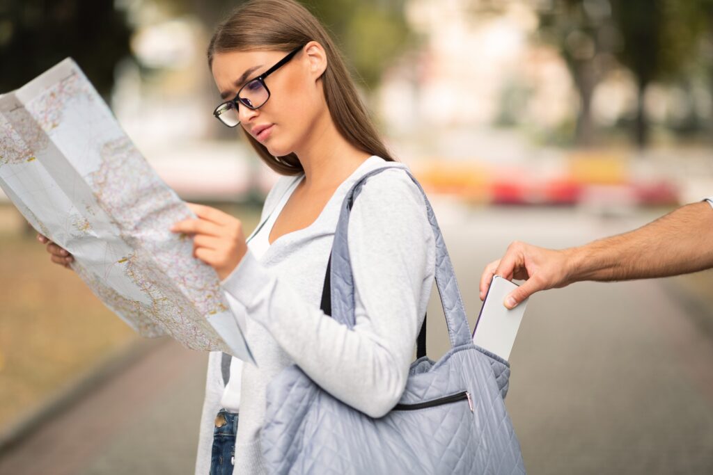 A young woman reading a map in a European city while someone tries to pickpocket her phone, a hand is seen reaching into her bag.