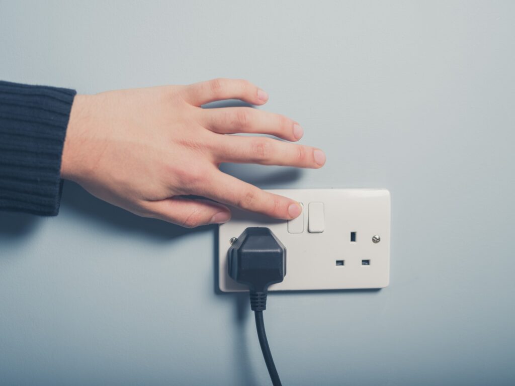 A simple photo of just a hand switching of a plug at the wall.